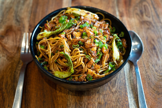 indian chinese spicy haka noodles with chicken tofu paneer with spices and cabbage placed in a black bowl on a wodden table ready to eat in a restaurant