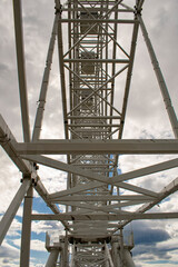 A giant construction of a Ferris wheel against a blue sky with clouds.