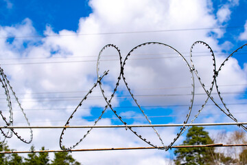 Spirally twisted barbed wire against the backdrop of clouds and blue sky.
