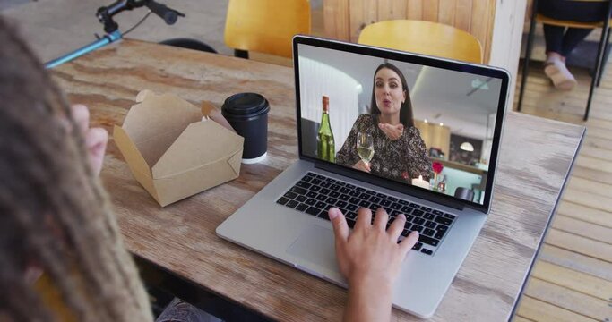 Woman having a snack while having a video call on laptop at cafe