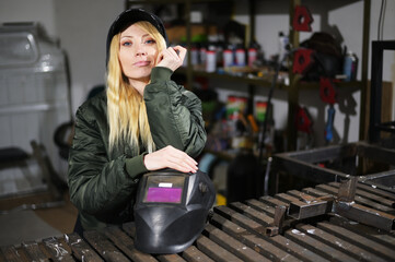 Portrait of a beautiful girl with a helmet of the welder posing in the garage