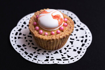 Brown cupcake with white meringue, lemon cream and pink candies, on white paper