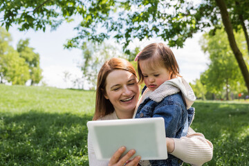 smiling woman holding autistic daughter and digital tablet in park