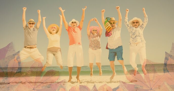 Composition of happy senior holiday group jumping raising hands, smiling on beach and autumn foliage
