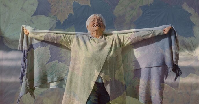 Composition of senior woman with arms wide, smiling on beach and autumn foliage