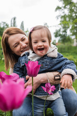 happy mother hugging daughter with disability near blurred flowers