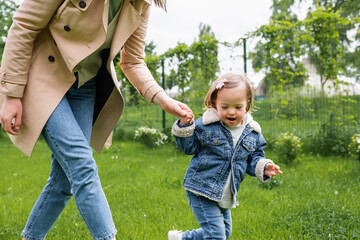 mother holding hands and walking with autistic daughter in park