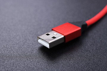 Detail of a red USB cable connector for a mobile phone on a black background.