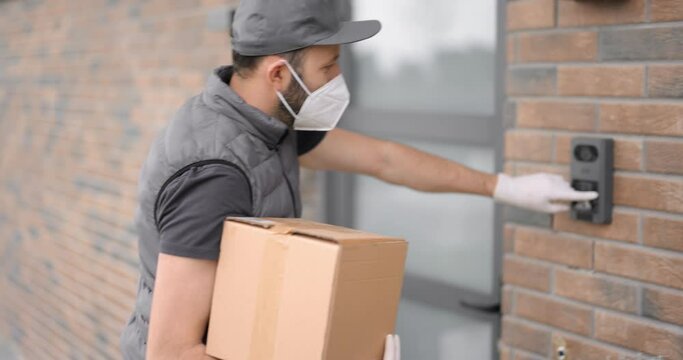 Courier in face mask delivers parcel for a young woman at the doorway of the house. Deliverying goods during a pandemic and happy customer concept
