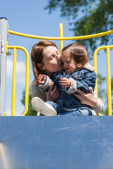 Fototapeta na wymiar woman kissing autistic girl on playground outdoors