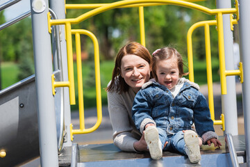 excited mother and autistic girl smiling at camera on playground