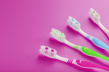 Four toothbrushes on a pink background in a row.