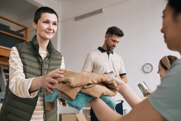 Portrait of mature woman giving used clothes to volunteers during help and donations event, copy space