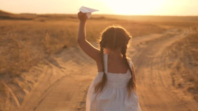 Happy child runs with toy airplane on background of sunset over field. girl runs with paper airplane in her hand. girl dreams of traveling. Kid dream of freedom, flight, kid play in field.