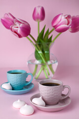 Fototapeta na wymiar A two cups of black coffee and a vase with bouquet pink tulip on the pink background. Close-up.
