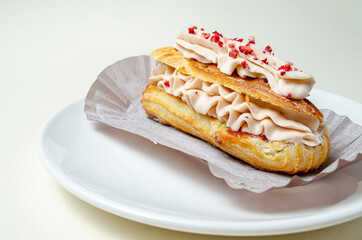 Eclair with cream and strawberries. On a white plate High quality photo