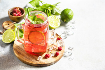 Soft drinks, healthy beverage. Refreshing summer glasses drink raspberry with mint lime and ice on a stone table. Copy space.