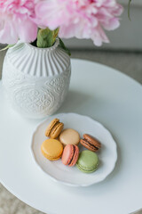 Living room interior. Bouquet of pink peonies in a vase, multicolored French macaroon pastries. Cozy. Spring.
