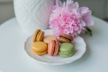 Living room interior. Bouquet of pink peonies in a vase, multicolored French macaroon pastries. Cozy. Spring.