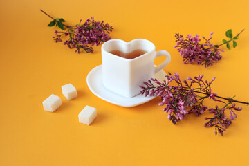 Obraz na płótnie Canvas A cup of tea with lilac branches, three sugar cubes on a yellow background, a side view-the concept of a good morning and the beginning of a good day.