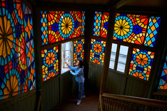 Cute brunette girl posing on authentic balcony of an old residential building with a stained glass window made of multicolored mosaics