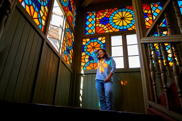 Cute brunette girl posing on authentic balcony of an old residential building with a stained glass...