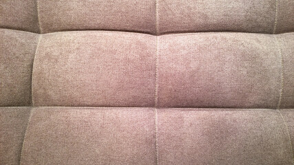 Fototapeta premium Detail of upholstery of modern chair, armchair, sofa, pouf or pillow. Brown color. Premium luxury fabric. Home decor. Design interior. Natural beige hue backdrop. Close-up. Furniture Manufacturing.