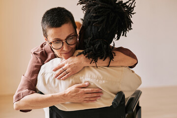 Minimal portrait of female psychologist embracing man in wheelchair during therapy session in...