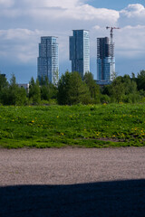 Obraz premium Three highrise buildings standing behing large bushes against cloydy sky.