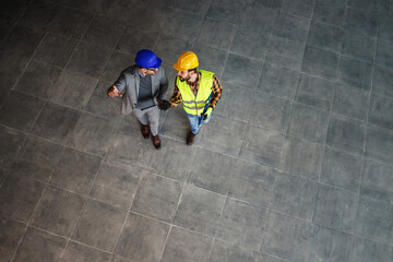 Aerial view of construction worker and architect walking on construction site and discussing about...