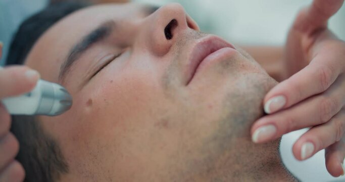 Close-up face of a male is laying while a cosmetologist is holding by one hand his face for non-injection mesotherapy procedure on his eyelid by using Dermadrop TDA device.