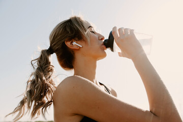 Athletic woman using earphones, takes a break and drinking water