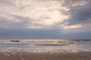 Sunset dramatic sky above washed up sea foam on the pristine Dutch North sea beach during on overcast day. Coastal weather and climate conditions concept.