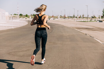 Back view of sports woman jogging on asphalt path during outdoor workout on sunny day