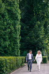 Fototapeta premium Loving groom and cute bride in suits with long hair are walking in nature. smiling newlyweds.