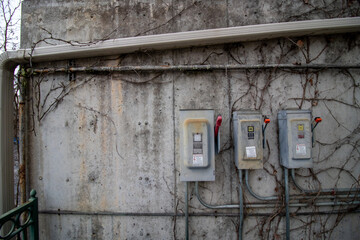 Fototapeta na wymiar Electrical meters on concrete stone wall with vines and bramble on back of shopping center on cloudy day in winter