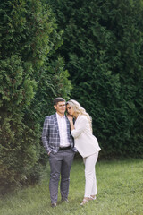 Stylish groom in a blue suit and a bride with curly hair hug in nature. smiling newlyweds against the backdrop of greenery.