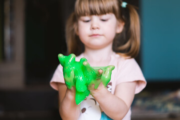 Green slime in children's hands. A little girl is playing with slime. The child squeezes the green slime through his fingers. Children's games, study, experiment. The concept of a happy, fun childhood