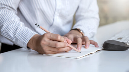Close-up of a man hand holding pencil taking notes on a blank white paper in the office.