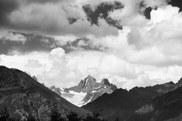 Black and white high rocky mountains with snow and glacier, sunlit sky with clouds at summer