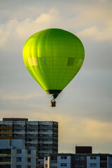 Fototapeta na wymiar Sunlit green hot air balloon on the sky over city buildings