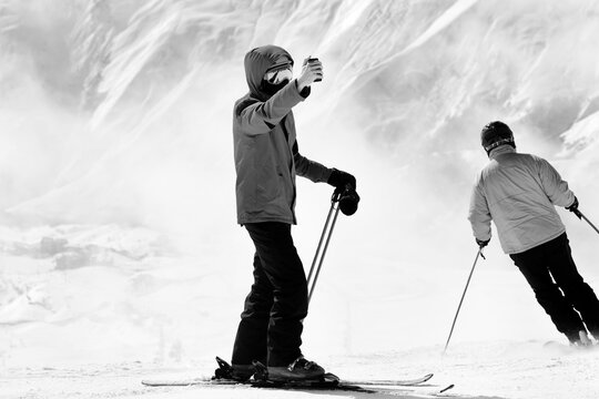 Skier makes selfie on camera phone and snow mountains in fog. Black and white toned image.