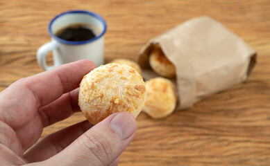 Hand holding typical brazilian cheese bun in front of unfocused breads and coffee cup