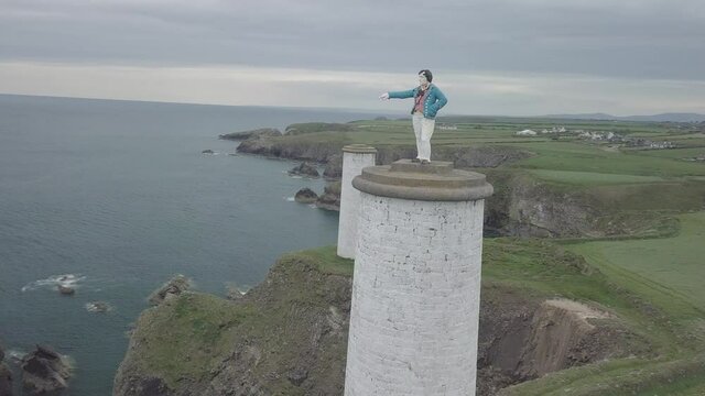 Vue a&eacute;rienne circulaire autour d'une statue pos&eacute;e sur une colonne.  C&ocirc;tes rocheuses entour&eacute;e de paysages verdoyants. Irlande 