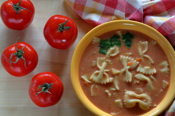 tomato soup in a bowl with four ripe tomatoes and linen cloth on wooden table top view