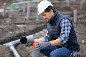 plumber fixing sewerage pipe at construction site - obrazy, fototapety, plakaty
