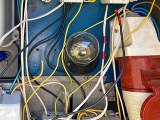 A light bulb in a homemade electric control cabinet for electronic devices with circuit breakers and counters in an iron box