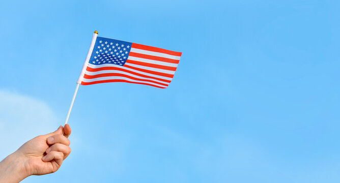 Hand holds USA flag on blue sky background.American symbol of Independence Day, Fourth of July, democracy and patriotism. Copy space fot text