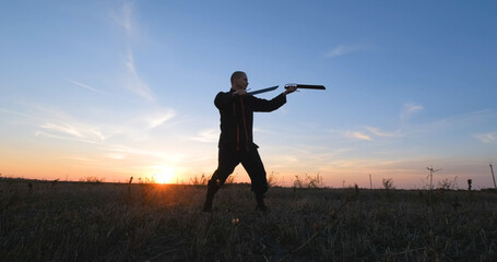 Silhouette of young male kung fu fighter practising alone in the fields during sunset	