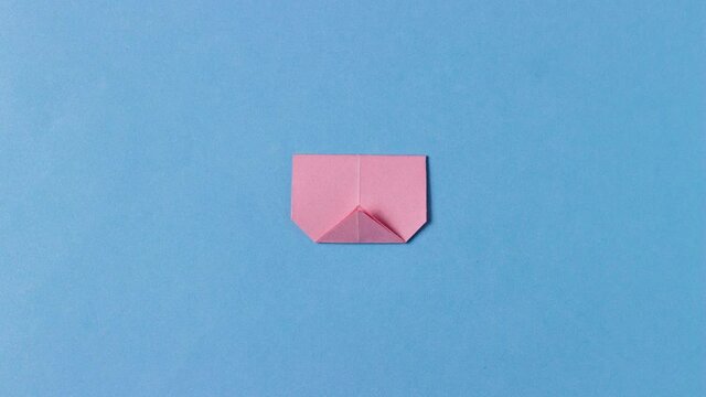 The pig's head from pink paper in the technique of origami with painted mustache unfolded on the blue background. Concept of love pets, farm, pastime, hobbies, activities with children.